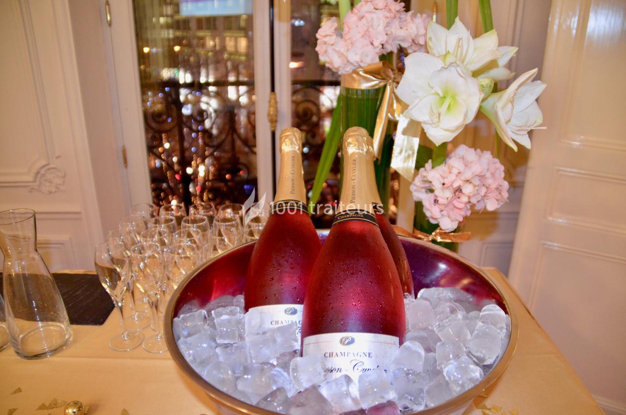 Deux bouteilles de champagne rosé dans un seau rempli de glace, entourées de fleurs et de verres à pied.