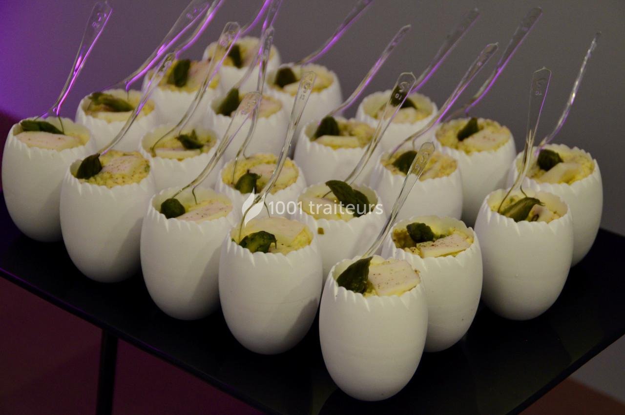 Des verrines en forme de coquilles d'œufs contenant une préparation garnie de feuilles vertes, servies avec des cuillères…