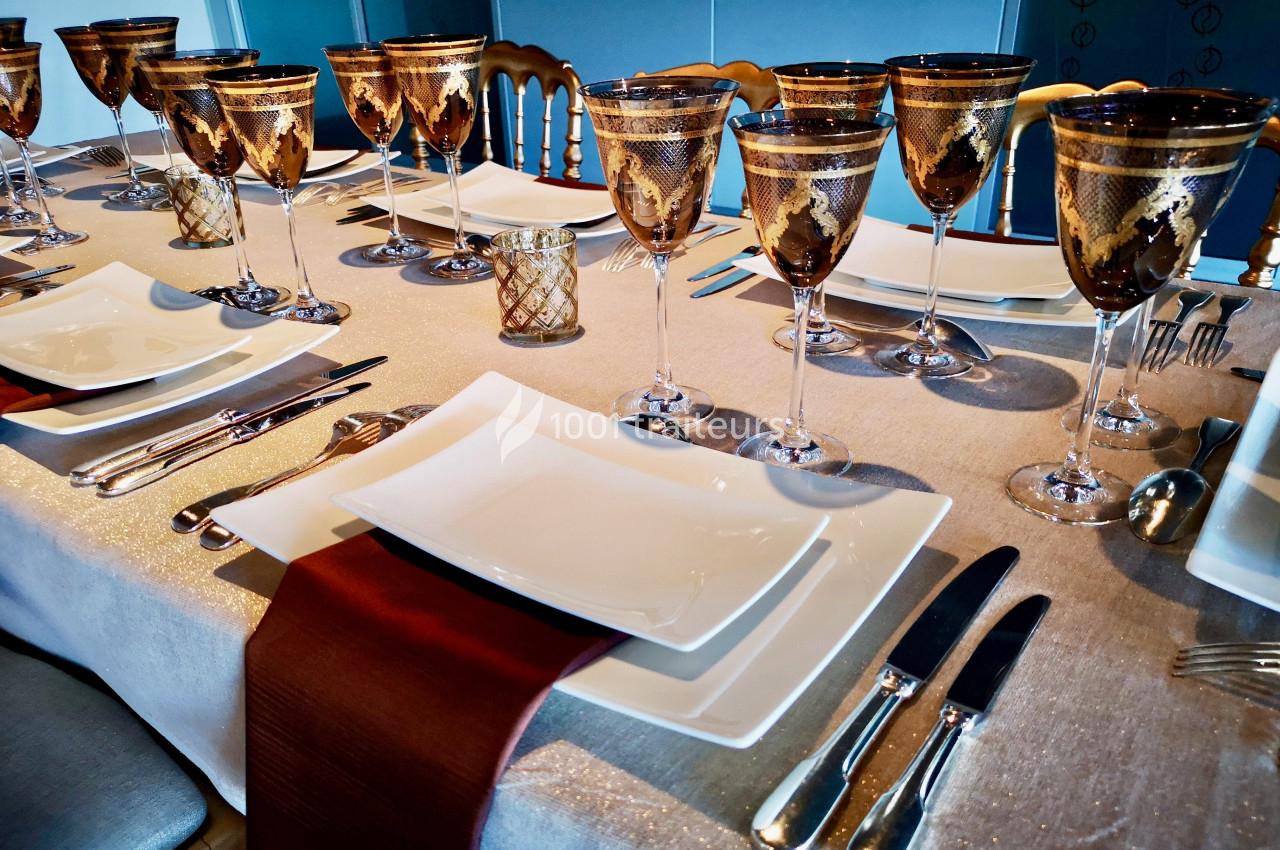 Table élégamment dressée avec nappes beige, assiettes blanches, verres dorés et couverts disposés symétriquement.
