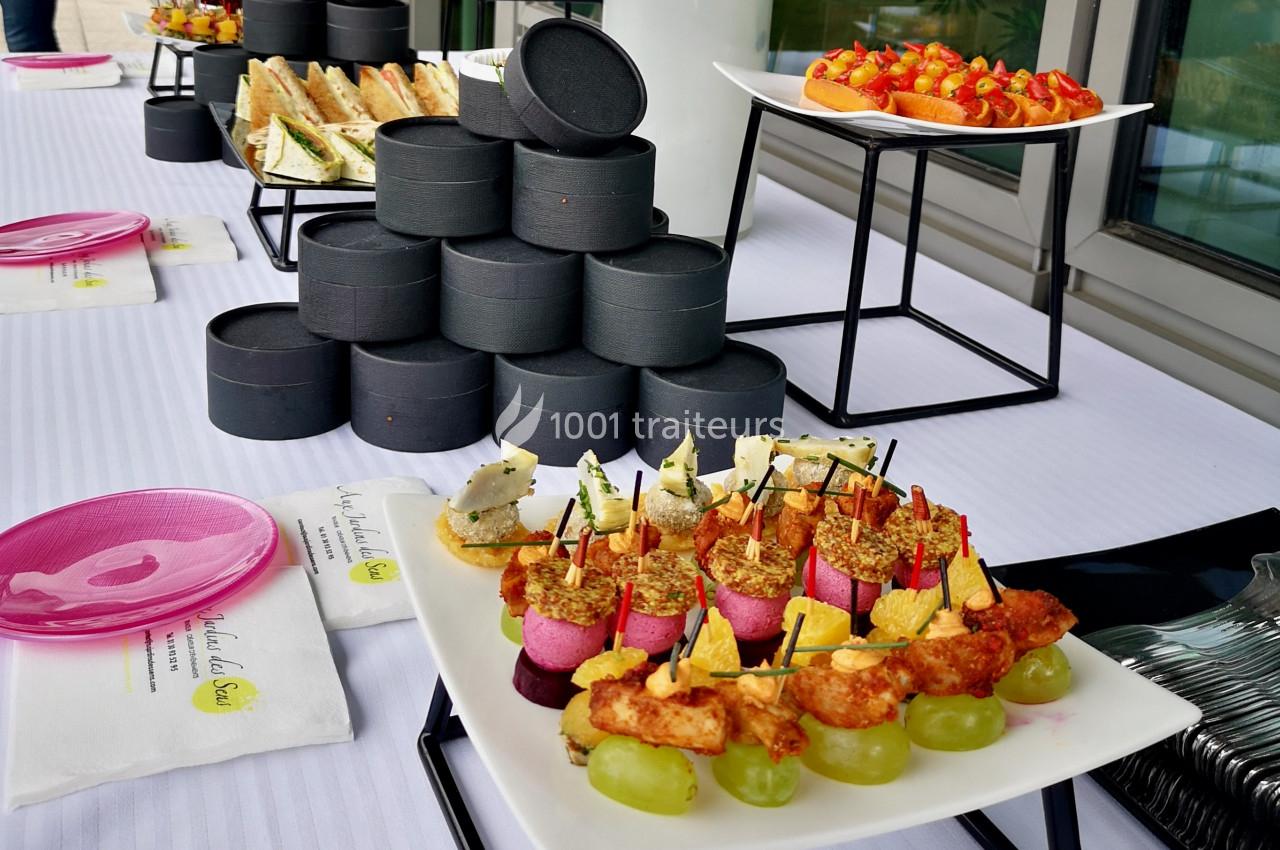 Plateau de bouchées apéritives variées disposées sur une table blanche avec des boîtes noires empilées en arrière-plan.