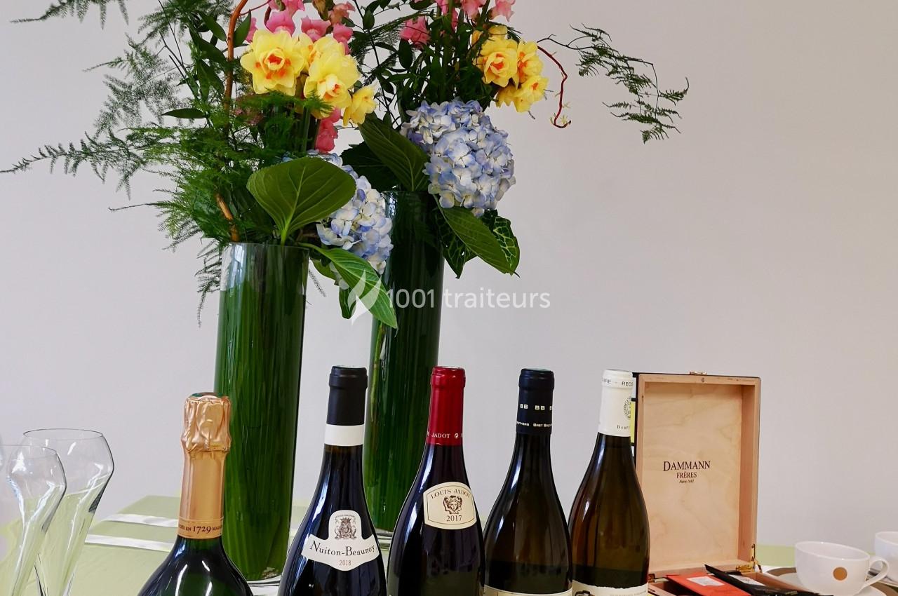 Bouteilles de vin et champagne alignées devant des vases contenant des fleurs colorées sur une table.