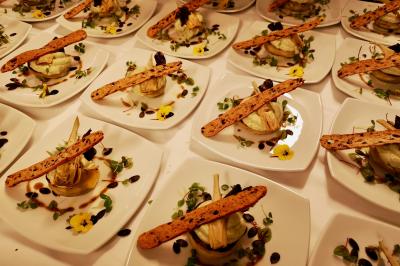 Façade illuminée d'un bâtiment élégant au crépuscule, avec un jardin et des invités rassemblés devant.