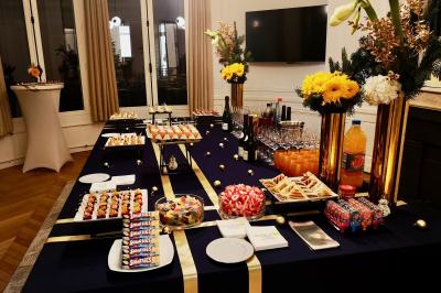 Façade illuminée d'un bâtiment élégant au crépuscule, avec un jardin et des invités rassemblés devant.