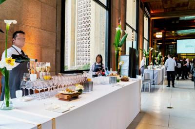 Façade illuminée d'un bâtiment élégant au crépuscule, avec un jardin et des invités rassemblés devant.