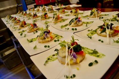 Façade illuminée d'un bâtiment élégant au crépuscule, avec un jardin et des invités rassemblés devant.
