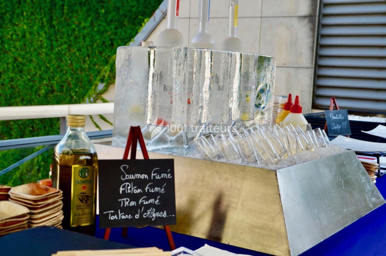 Stand de buffet avec blocs de glace contenant des bouteilles, ardoises indiquant des plats et huile d'olive en arrière-plan.