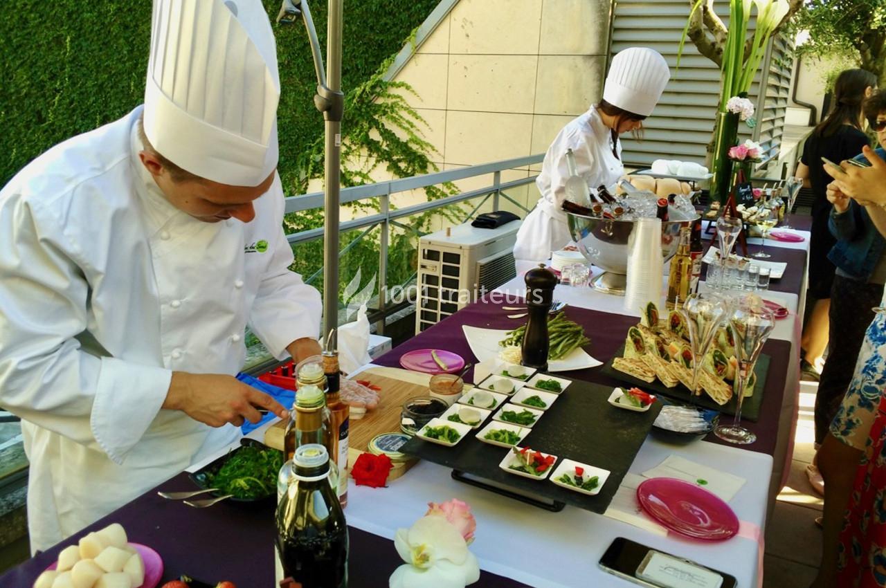 Un chef en tenue blanche prépare des plats sur une table garnie d'ingrédients et de décorations culinaires.