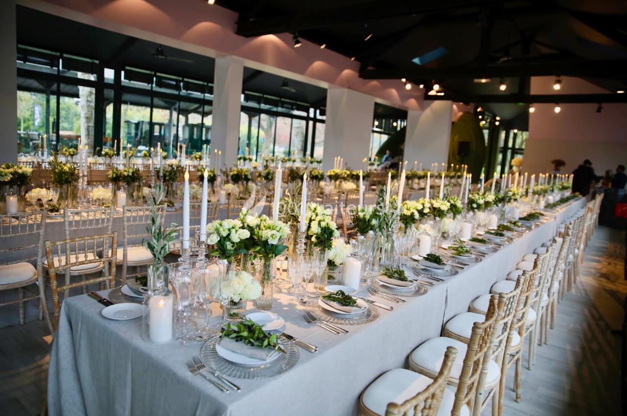 Salle de réception décorée avec des tables élégantes, chandeliers, fleurs blanches et chaises en bois clair.