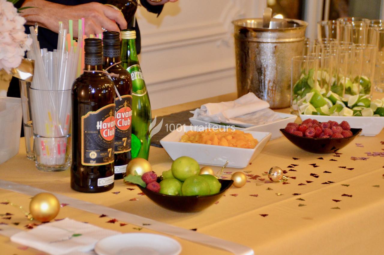 Table dressée avec des bouteilles, fruits frais, glaçons et décorations festives pour préparer des cocktails.