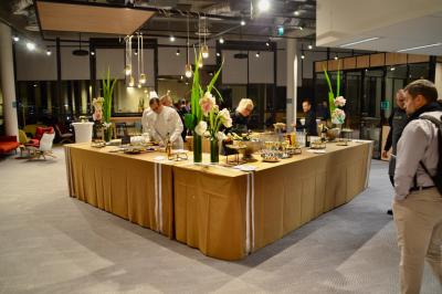 Façade illuminée d'un bâtiment élégant au crépuscule, avec un jardin et des invités rassemblés devant.