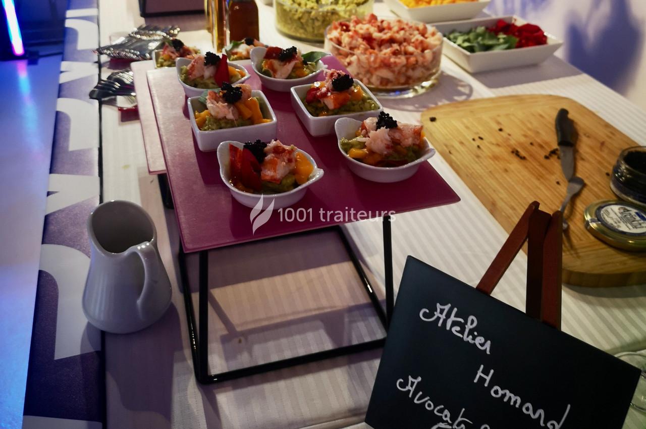 Plateau de verrines garnies de homard et avocat, entouré d'autres plats et d'une ardoise descriptive.