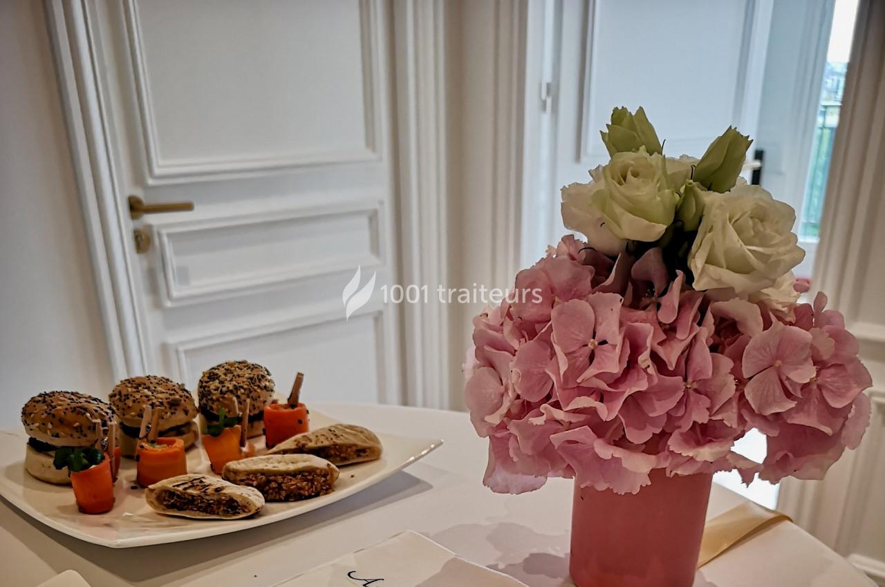 Assiette de mini-sandwichs et légumes en apéritif sur une table, avec un bouquet de fleurs roses et blanches au premier plan.