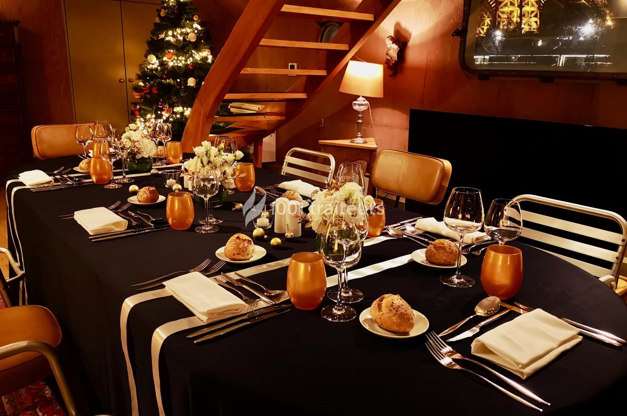 Table élégamment dressée avec nappe noire, décorations festives, bougies et sapin de Noël en arrière-plan.