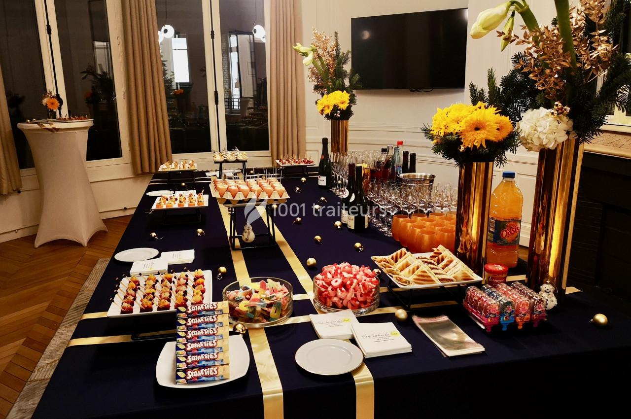 Table de buffet élégamment dressée avec desserts, boissons, fleurs jaunes et décorations festives sur une nappe bleue.