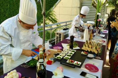Façade illuminée d'un bâtiment élégant au crépuscule, avec un jardin et des invités rassemblés devant.