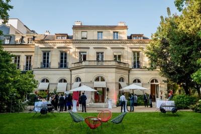 Façade illuminée d'un bâtiment élégant au crépuscule, avec un jardin et des invités rassemblés devant.