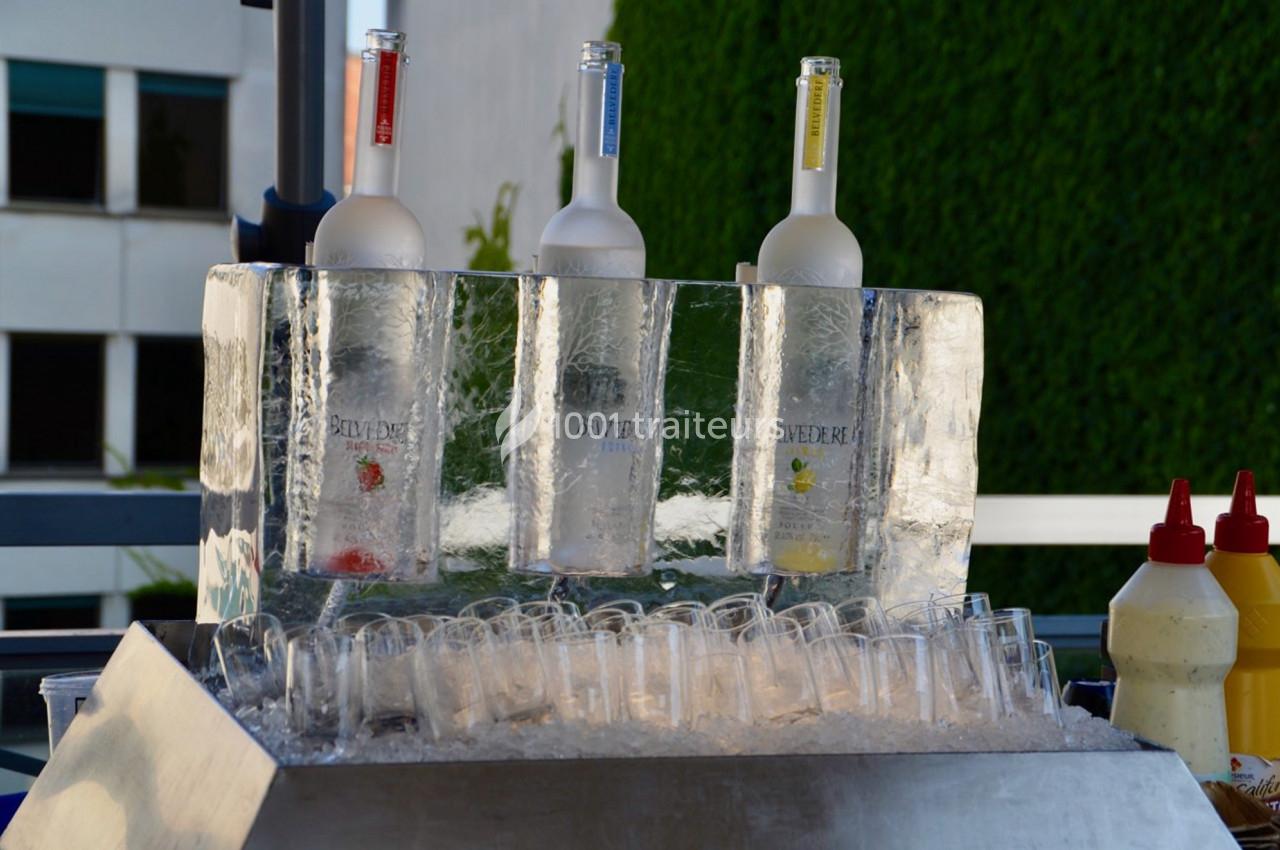 Bouteilles de vodka glacées disposées dans un présentoir en glace avec des verres alignés en dessous.