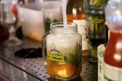 Un cocktail en préparation dans un verre en mason jar, avec des feuilles de menthe et des ingrédients visibles en arrière…