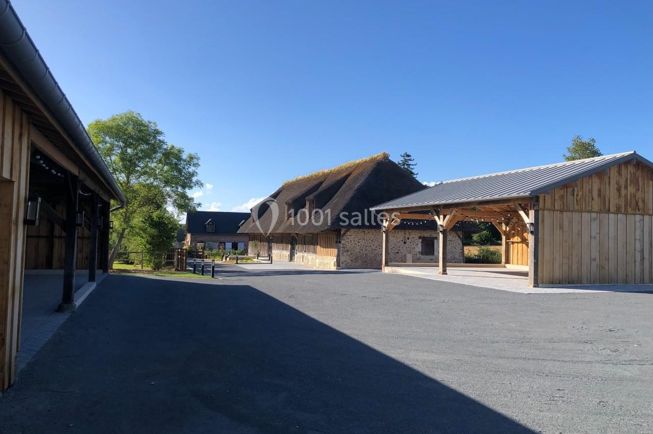 Cour avec bâtiments en bois et en pierre, dont une maison à toit de chaume, sous un ciel dégagé.