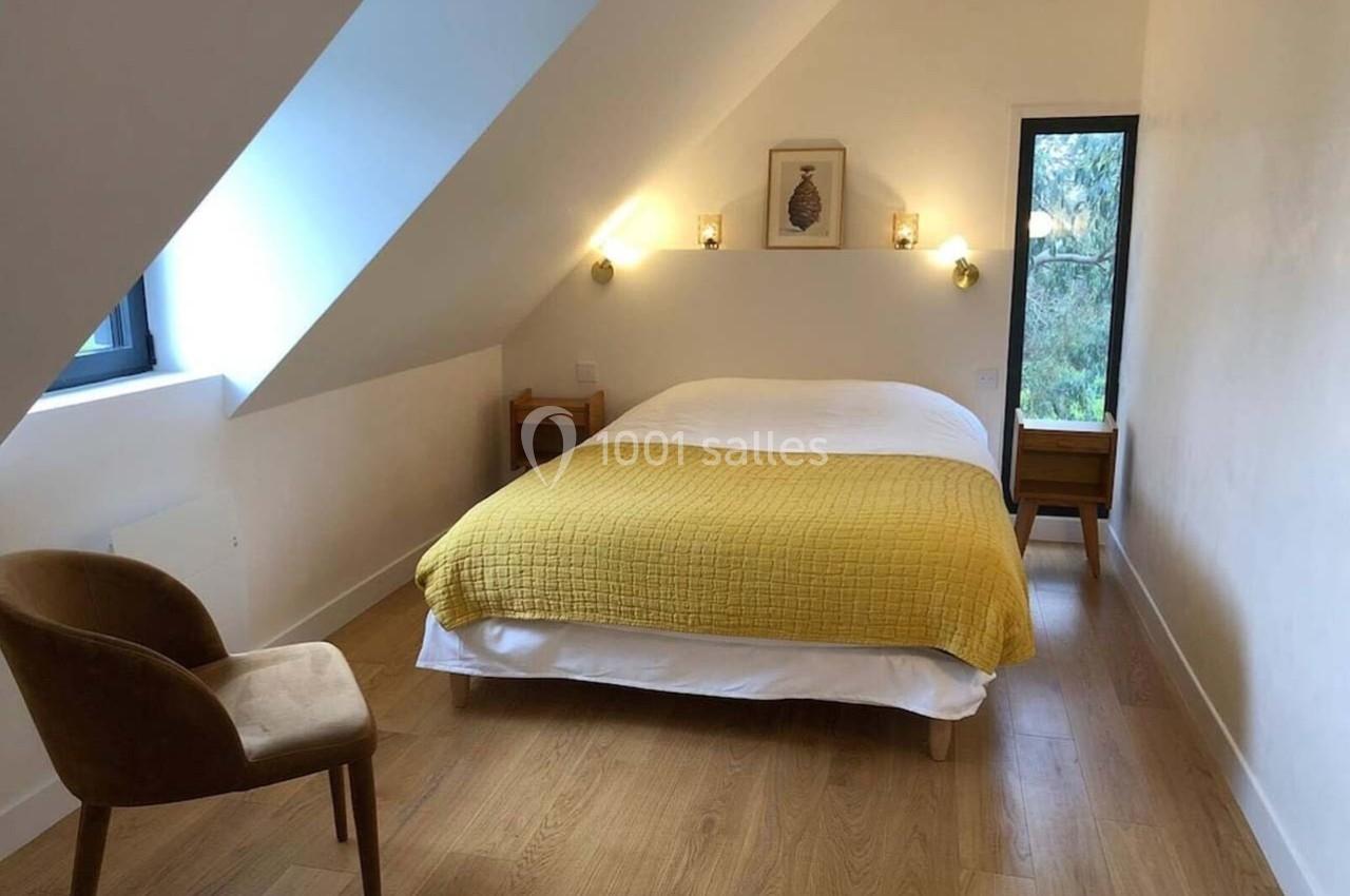 Chambre lumineuse avec lit double, couvre-lit jaune, murs blancs, parquet clair et fenêtre donnant sur un jardin.