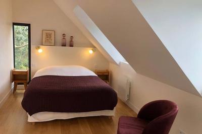 Chambre mansardée avec mur en briques, lit avec coussins, parquet clair et lumière naturelle provenant de deux fenêtres de…