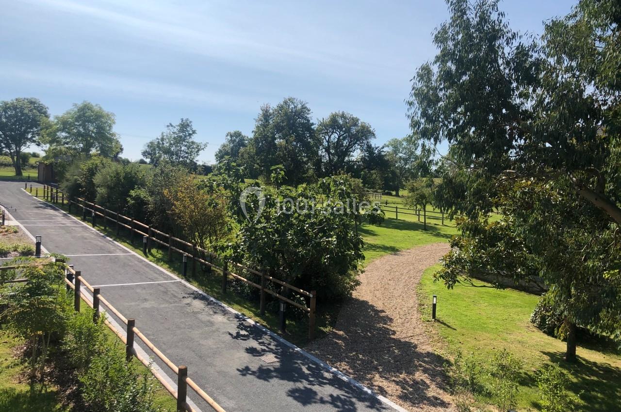 Chemin asphalté bordé de clôtures en bois, entouré d'arbres et de pelouses sous un ciel dégagé.