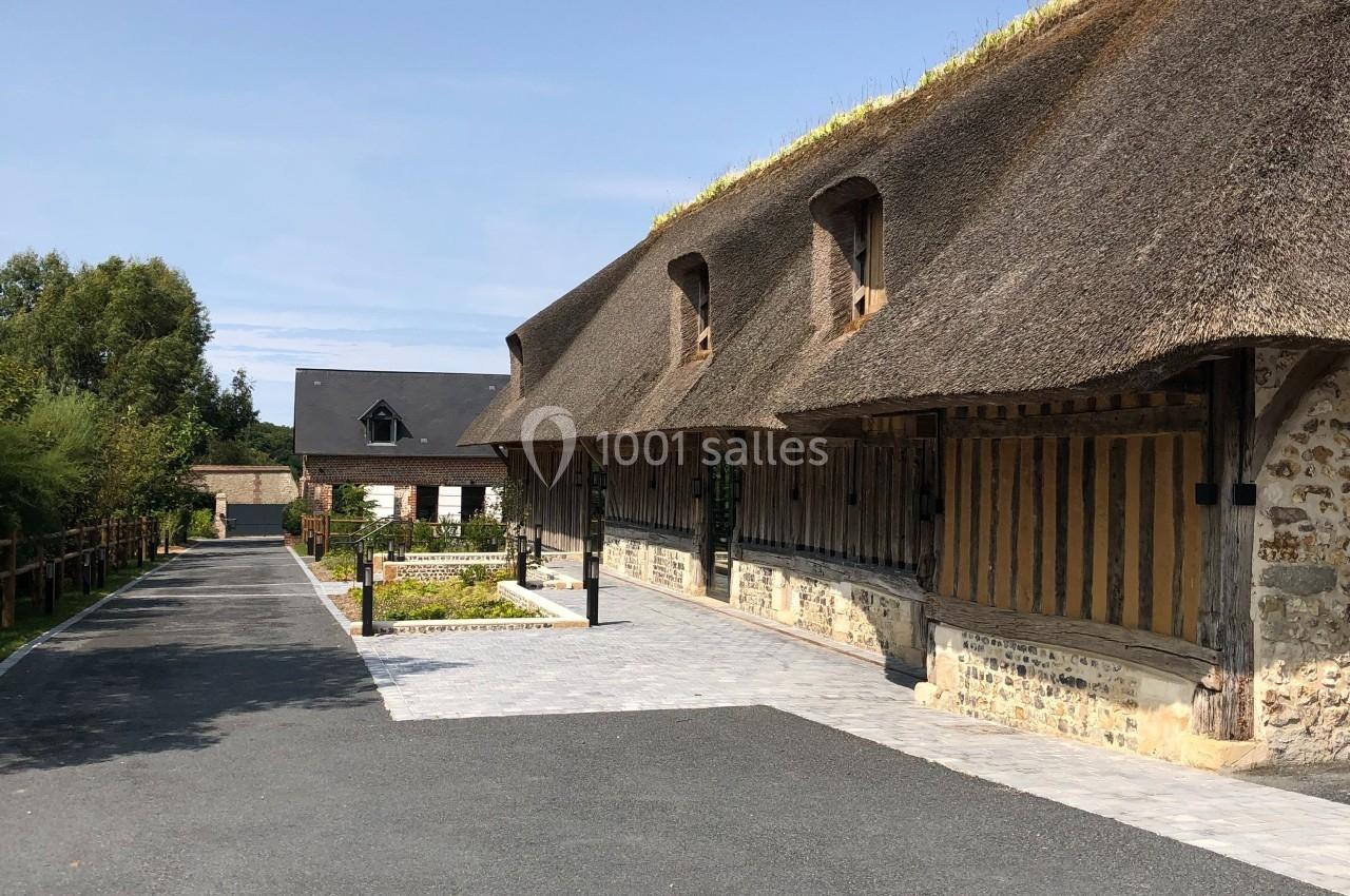 Bâtiment traditionnel à toit de chaume avec façade en colombages, bordé d'une allée pavée et d'espaces verts.