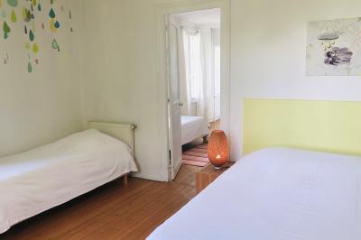 Chambre mansardée avec mur en briques, lit avec coussins, parquet clair et lumière naturelle provenant de deux fenêtres de…