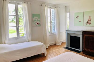 Chambre mansardée avec mur en briques, lit avec coussins, parquet clair et lumière naturelle provenant de deux fenêtres de…