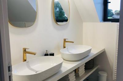 Chambre mansardée avec mur en briques, lit avec coussins, parquet clair et lumière naturelle provenant de deux fenêtres de…