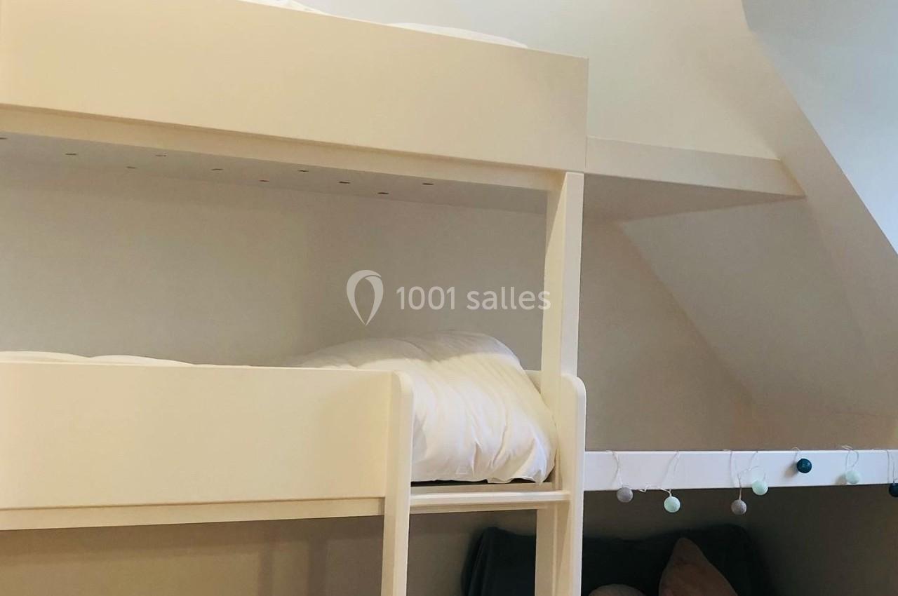 Lit superposé blanc avec échelle, accompagné d'une alcôve aménagée avec coussins et guirlande lumineuse.