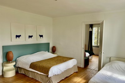 Miniature Gite La Ferme Chambre mansardée avec mur en briques, lit avec coussins, parquet clair et lumière naturelle provenant de deux fenêtres de…