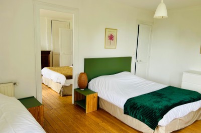 Miniature Gite La Ferme Chambre mansardée avec mur en briques, lit avec coussins, parquet clair et lumière naturelle provenant de deux fenêtres de…