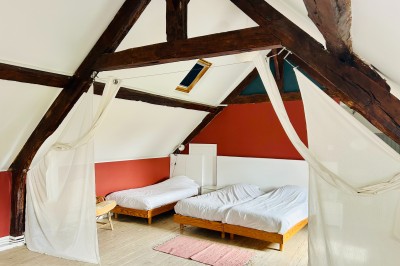 Miniature Gite La Ferme Chambre mansardée avec mur en briques, lit avec coussins, parquet clair et lumière naturelle provenant de deux fenêtres de…