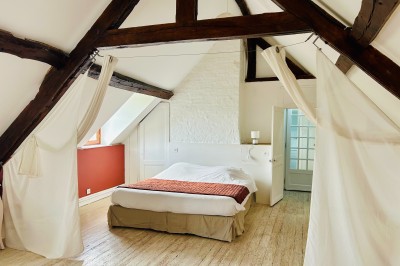Miniature Gite La Ferme Chambre mansardée avec mur en briques, lit avec coussins, parquet clair et lumière naturelle provenant de deux fenêtres de…