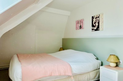 Miniature Gite La Ferme Chambre mansardée avec mur en briques, lit avec coussins, parquet clair et lumière naturelle provenant de deux fenêtres de…