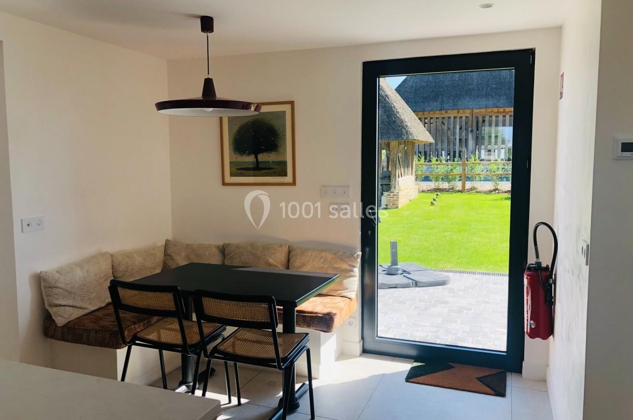Coin repas lumineux avec table, chaises, banquette, et porte vitrée donnant sur un jardin verdoyant.
