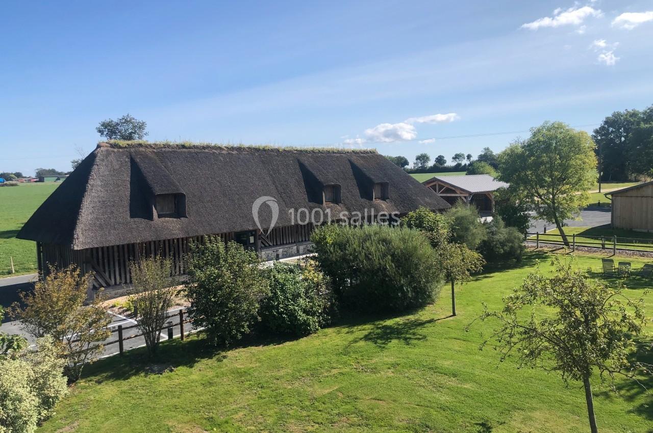 Bâtiment traditionnel au toit de chaume entouré de verdure, avec un ciel bleu dégagé en arrière-plan.