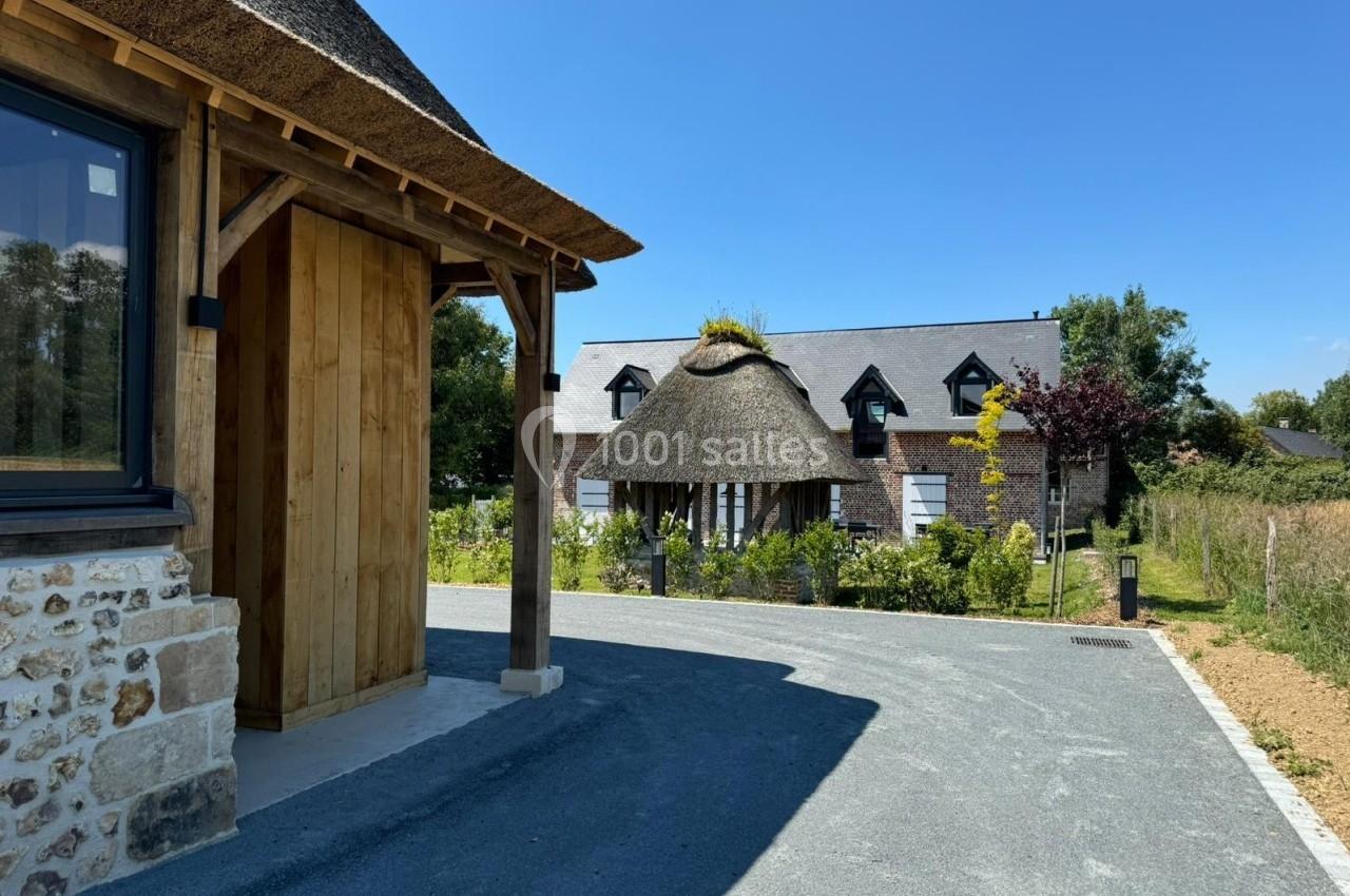 Maison en pierre et bois avec toit de chaume, entourée de végétation, vue depuis une allée pavée sous un ciel dégagé.
