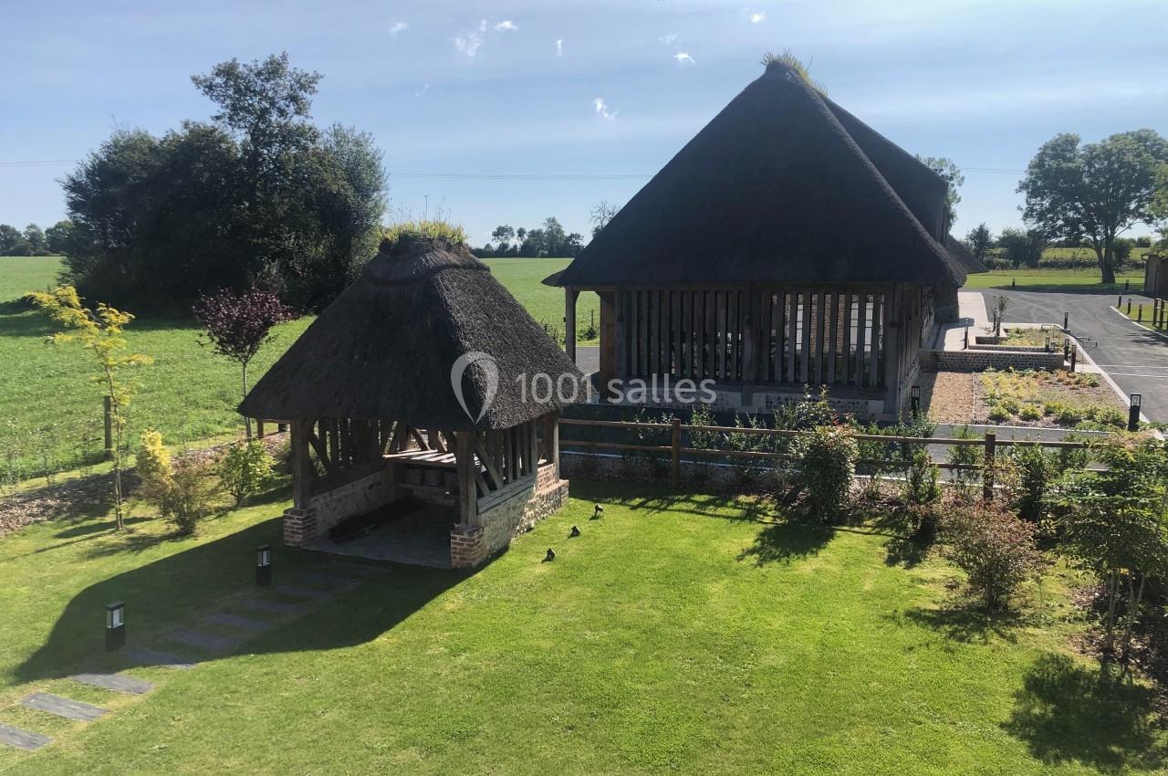Deux pavillons en toit de chaume entourés de pelouses et jardins, situés dans un paysage rural ensoleillé.