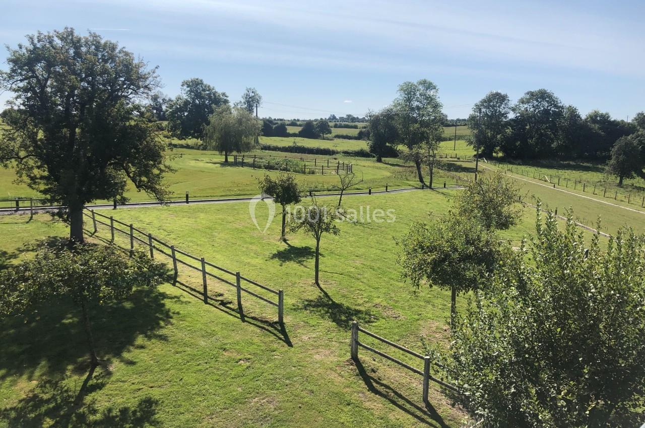Paysage champêtre avec des arbres clairsemés, des clôtures en bois et des prairies verdoyantes sous un ciel dégagé.