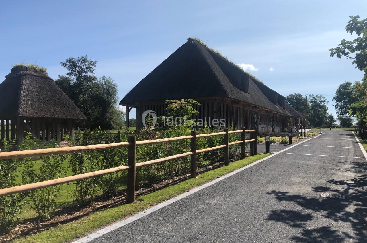 Bâtiments traditionnels en bois avec toits de chaume, entourés de verdure et longés par une route pavée.