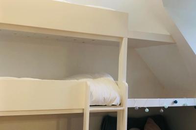 Chambre mansardée avec mur en briques, lit avec coussins, parquet clair et lumière naturelle provenant de deux fenêtres de…