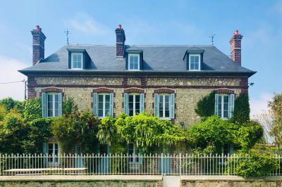 Chambre mansardée avec mur en briques, lit avec coussins, parquet clair et lumière naturelle provenant de deux fenêtres de…