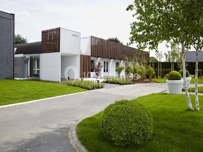 Bâtiment moderne entouré de pelouses bien entretenues, d'arbres et de grands pots de fleurs blanches.