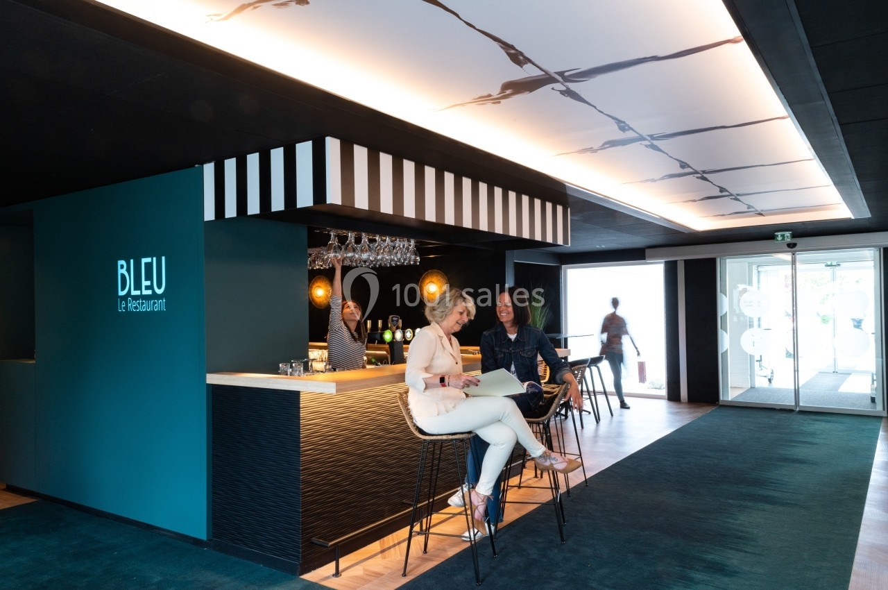 Deux femmes assises au bar d'un restaurant moderne avec un barman en arrière-plan.