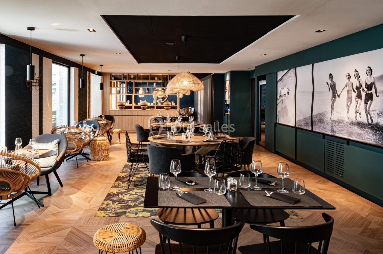 Salle de restaurant moderne avec tables dressées, chaises en rotin et décoration élégante dans des tons sombres et boisés.