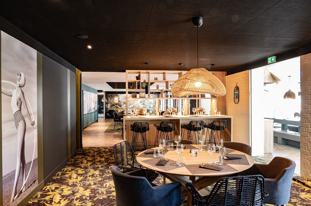 Salle de restaurant moderne avec table ronde dressée, bar en arrière-plan et décoration contemporaine.