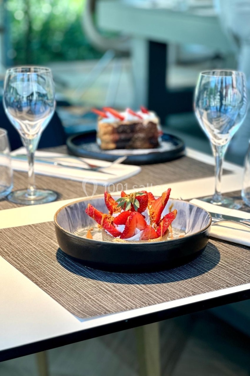 Assiette de dessert garnie de fraises fraîches sur une table dressée avec verres et couverts dans un cadre lumineux.