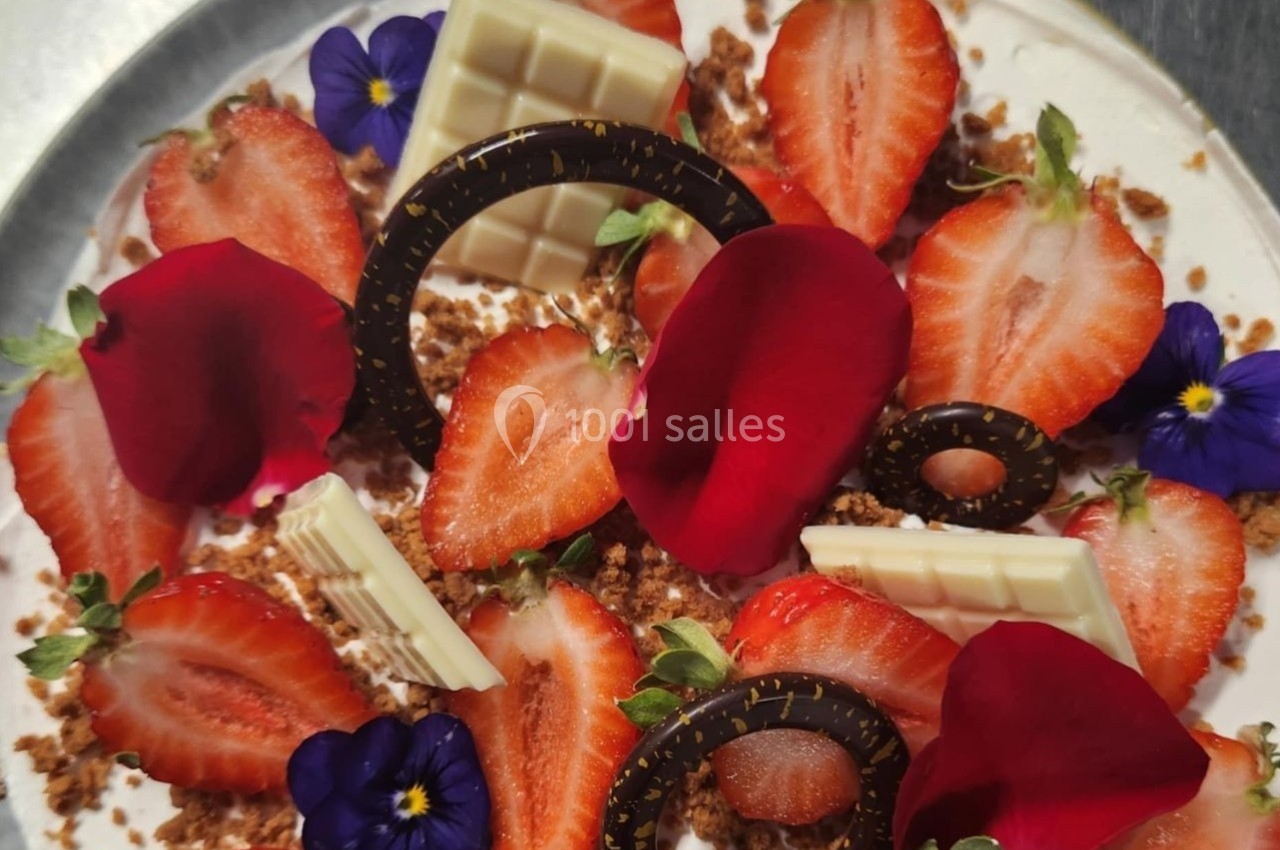 Dessert décoré de fraises, pétales rouges, fleurs comestibles, chocolat blanc et noir sur une base crémeuse.